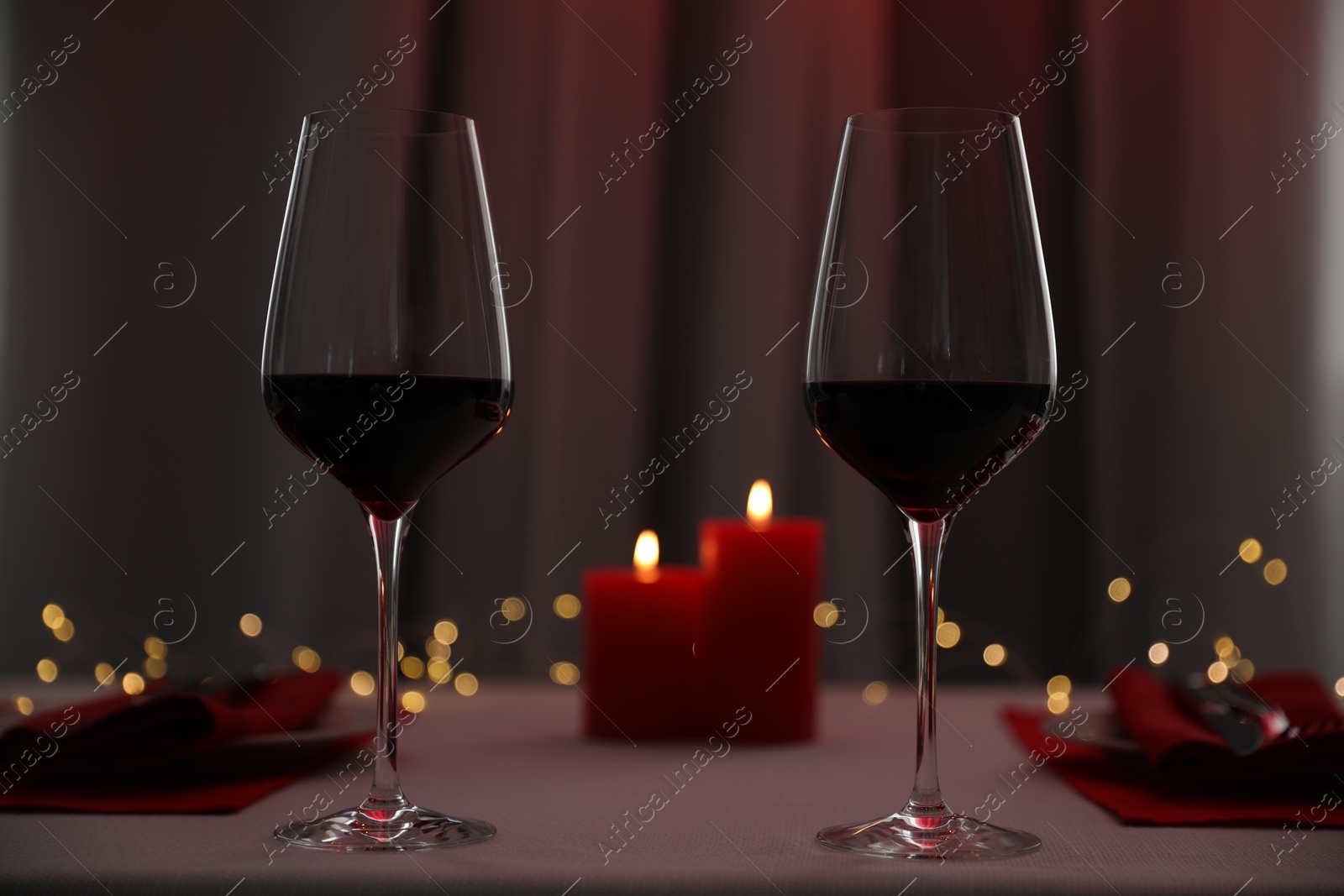 Photo of Burning candles and wine in glasses on table indoors. Bokeh effect