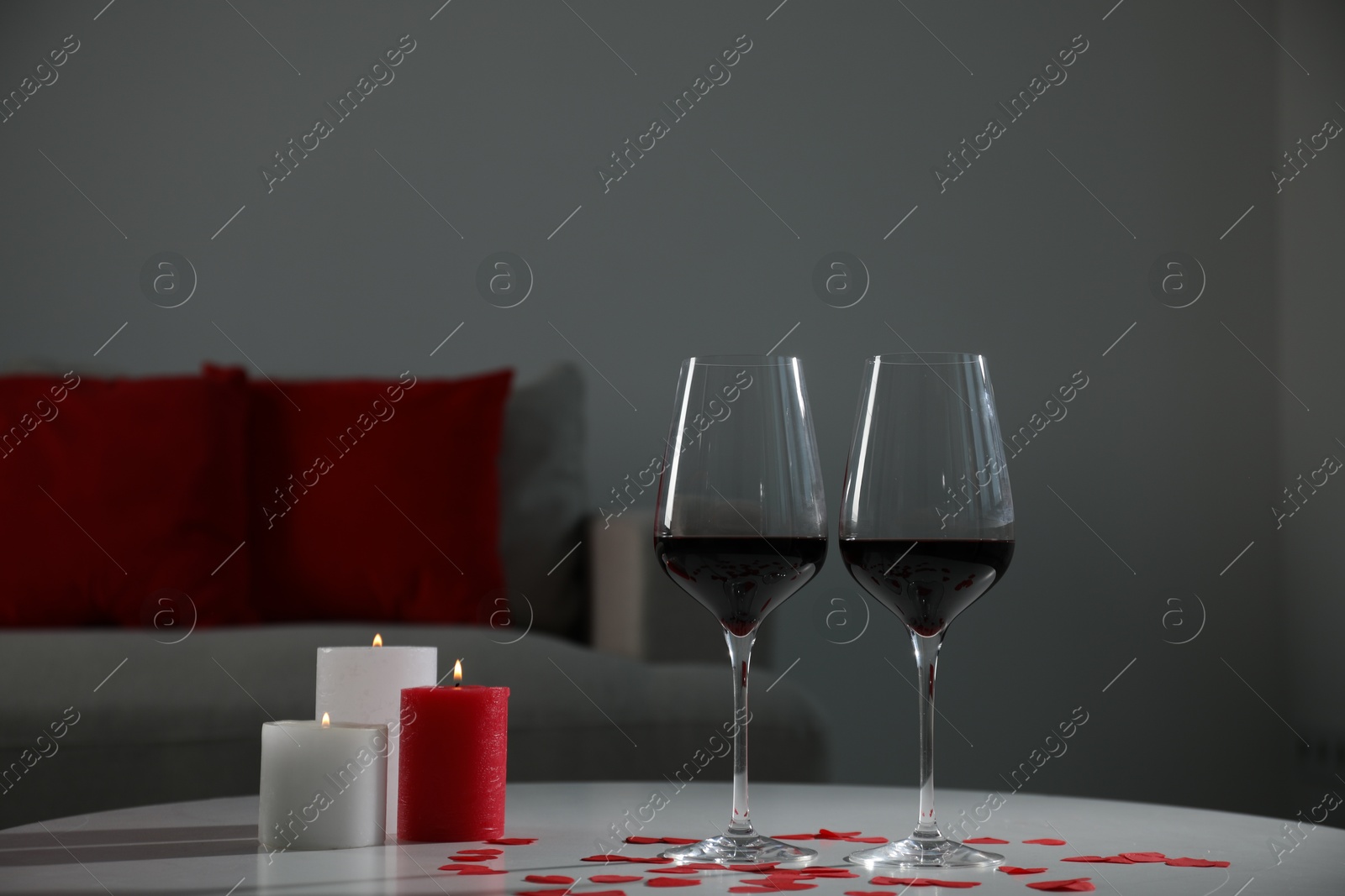 Photo of Burning candles, wine in glasses and paper hearts on table indoors