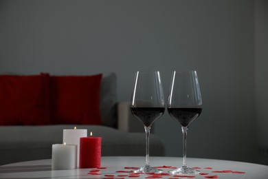 Burning candles, wine in glasses and paper hearts on table indoors