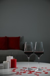 Burning candles, wine in glasses and paper hearts on table indoors