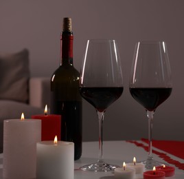 Burning candles, wine and paper hearts on table indoors