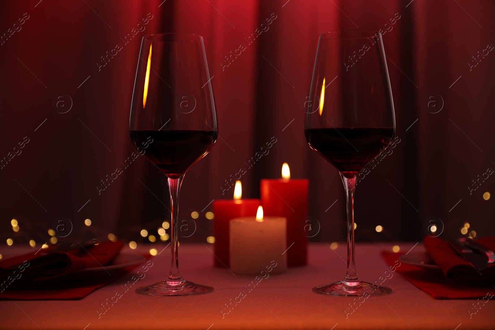 Photo of Burning candles and wine in glasses on table indoors