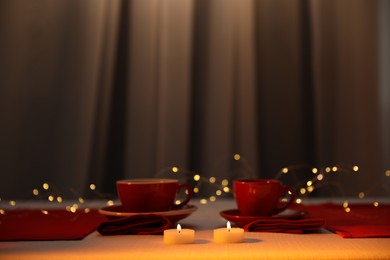 Photo of Burning candles and cups on table indoors. Bokeh effect