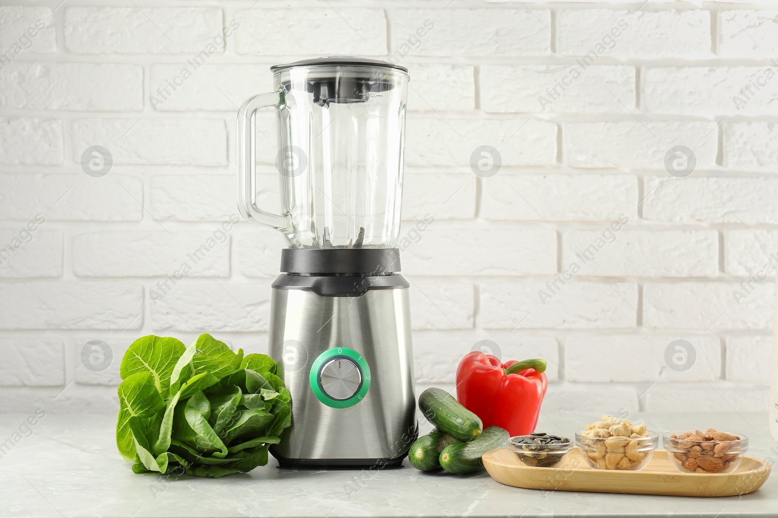 Photo of Blender and products on light table against white brick wall