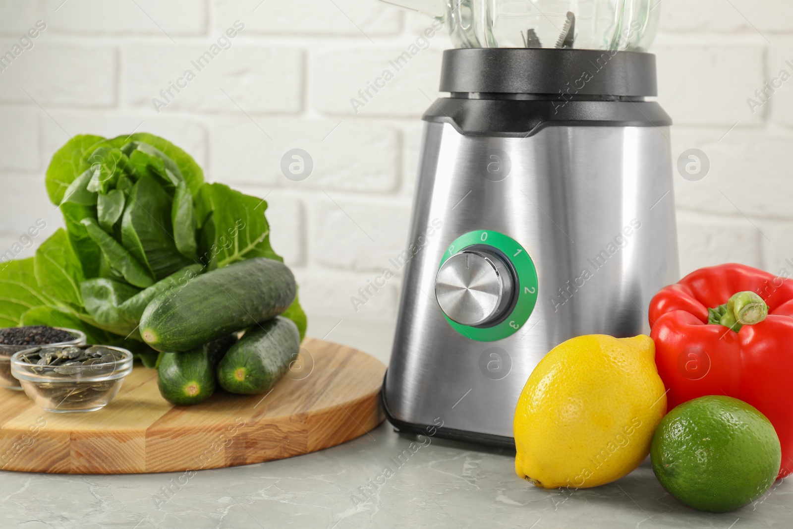 Photo of Blender and products on grey table against white brick wall, closeup