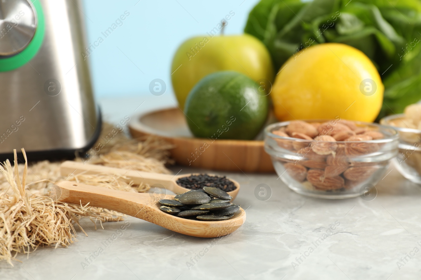 Photo of Spoons with seeds, blender and products on grey table, closeup