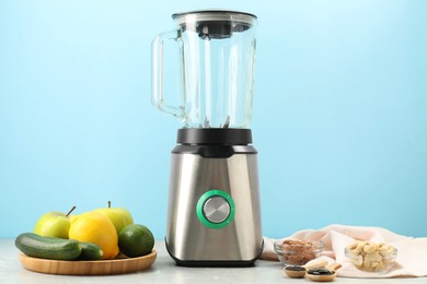 Blender and products on grey table against light blue background