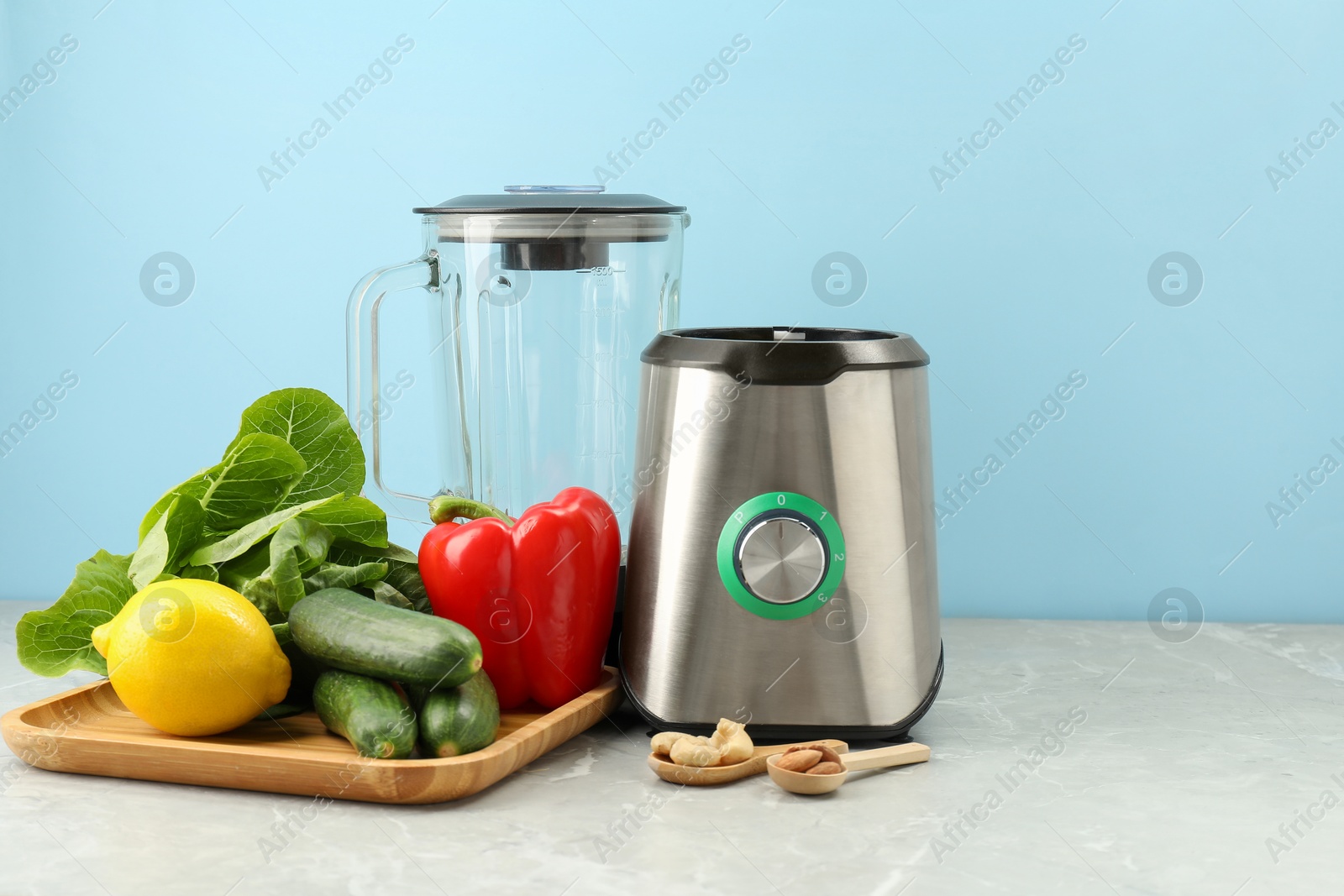 Photo of Blender and products on grey table against light blue background