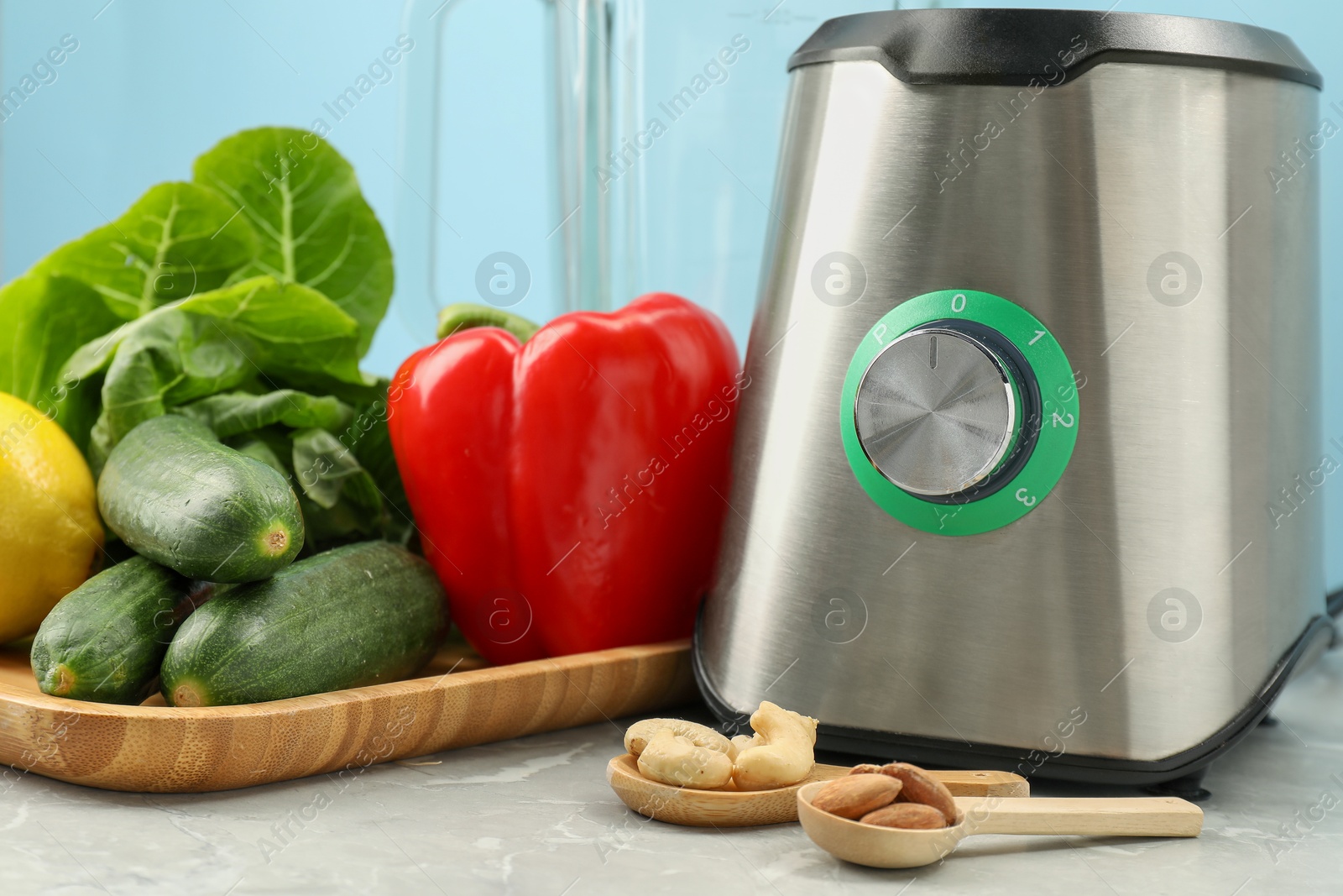 Photo of Blender, spoons with nuts and products on grey table against light blue background, closeup