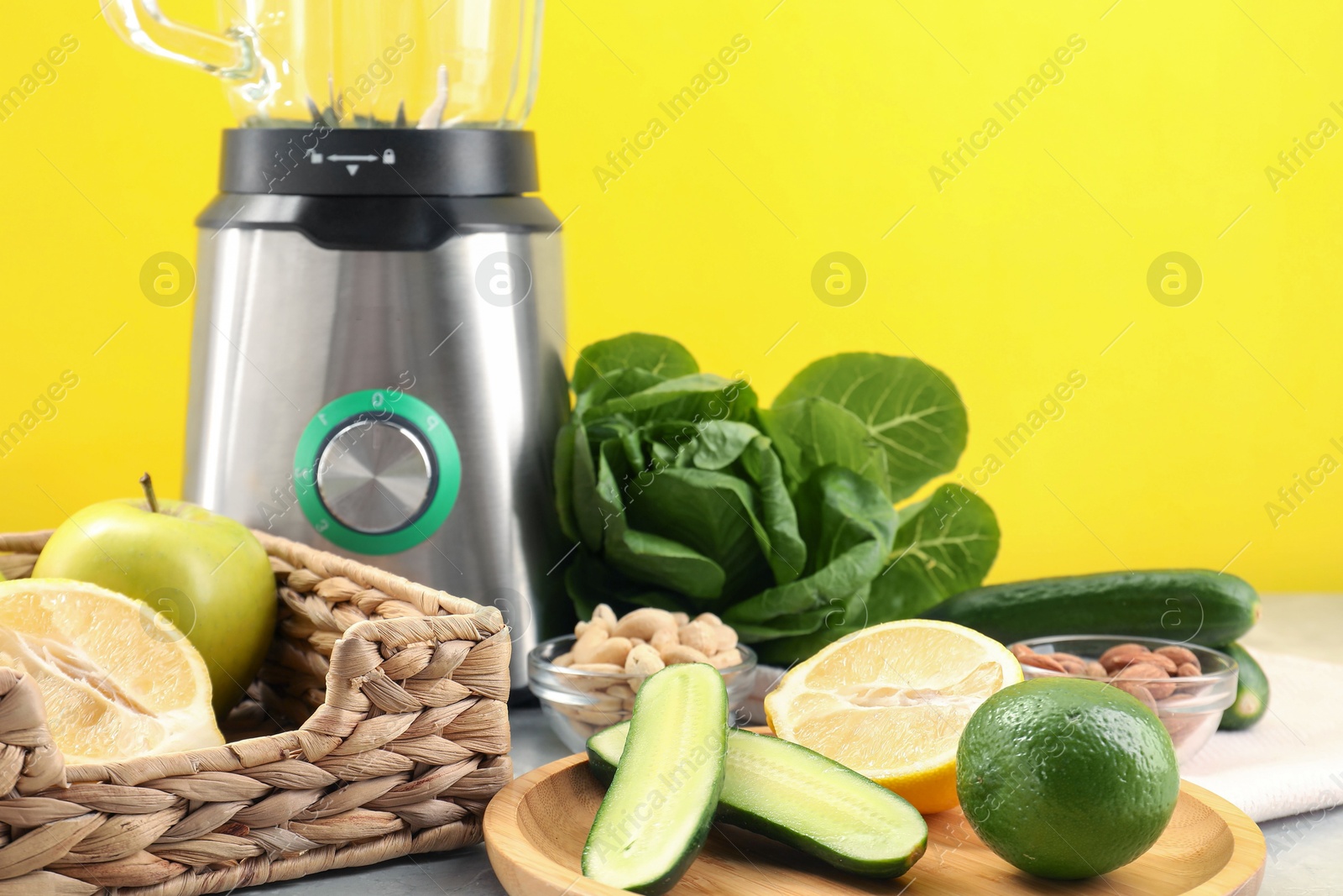 Photo of Blender and products on grey table against yellow background, closeup