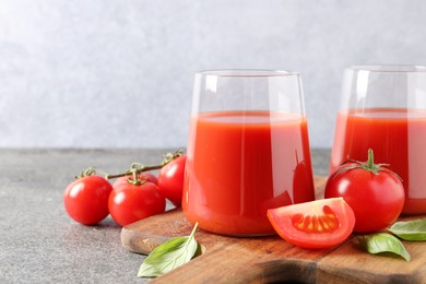 Photo of Tasty tomato juice in glasses, basil and fresh vegetables on grey table. Space for text