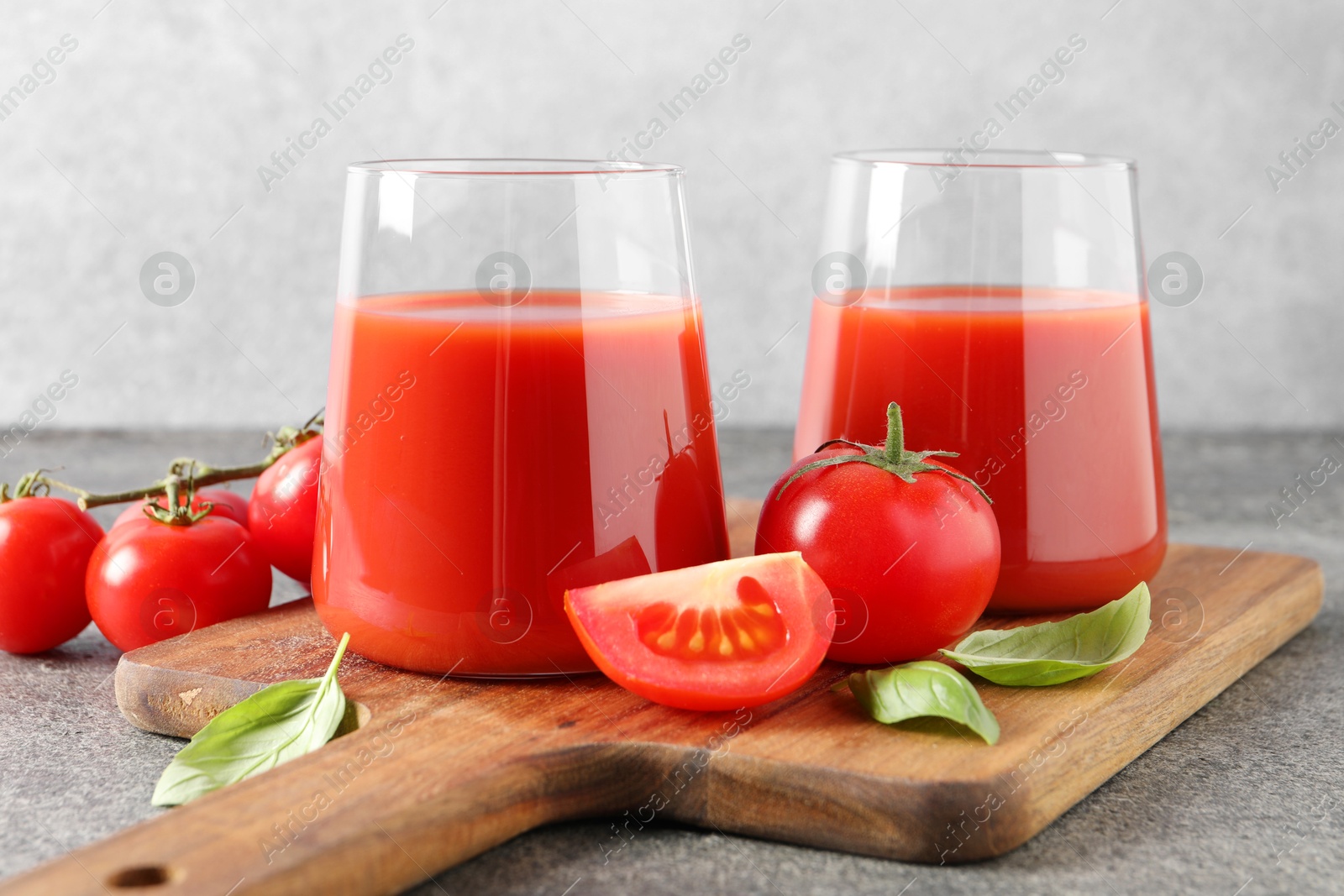 Photo of Tasty tomato juice in glasses, basil and fresh vegetables on grey table