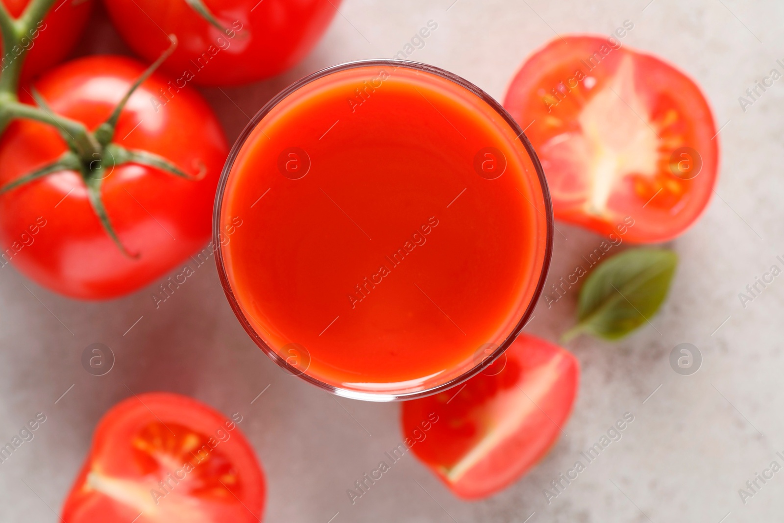 Photo of Tasty tomato juice in glass, basil and fresh vegetables on light grey table, top view