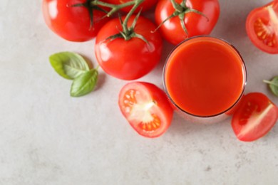 Tasty tomato juice in glass, basil leaves and fresh vegetables on light grey table, flat lay. Space for text