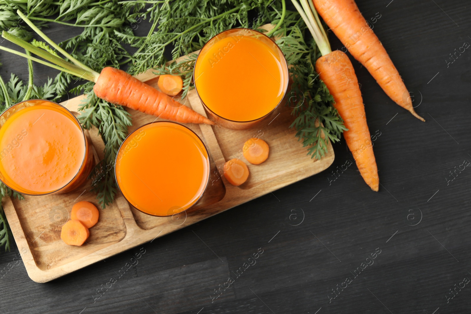 Photo of Healthy carrot juice in glasses and fresh vegetables on black wooden table, top view