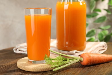 Photo of Healthy carrot juice in glass, bottle and fresh vegetable on wooden table