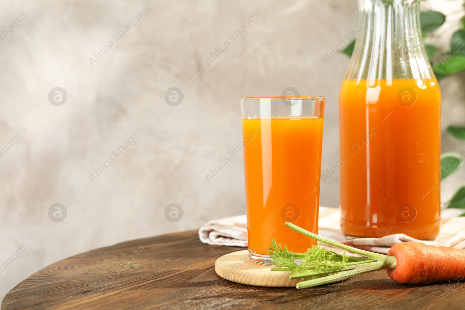 Photo of Healthy carrot juice in glass, bottle and fresh vegetable on wooden table, space for text