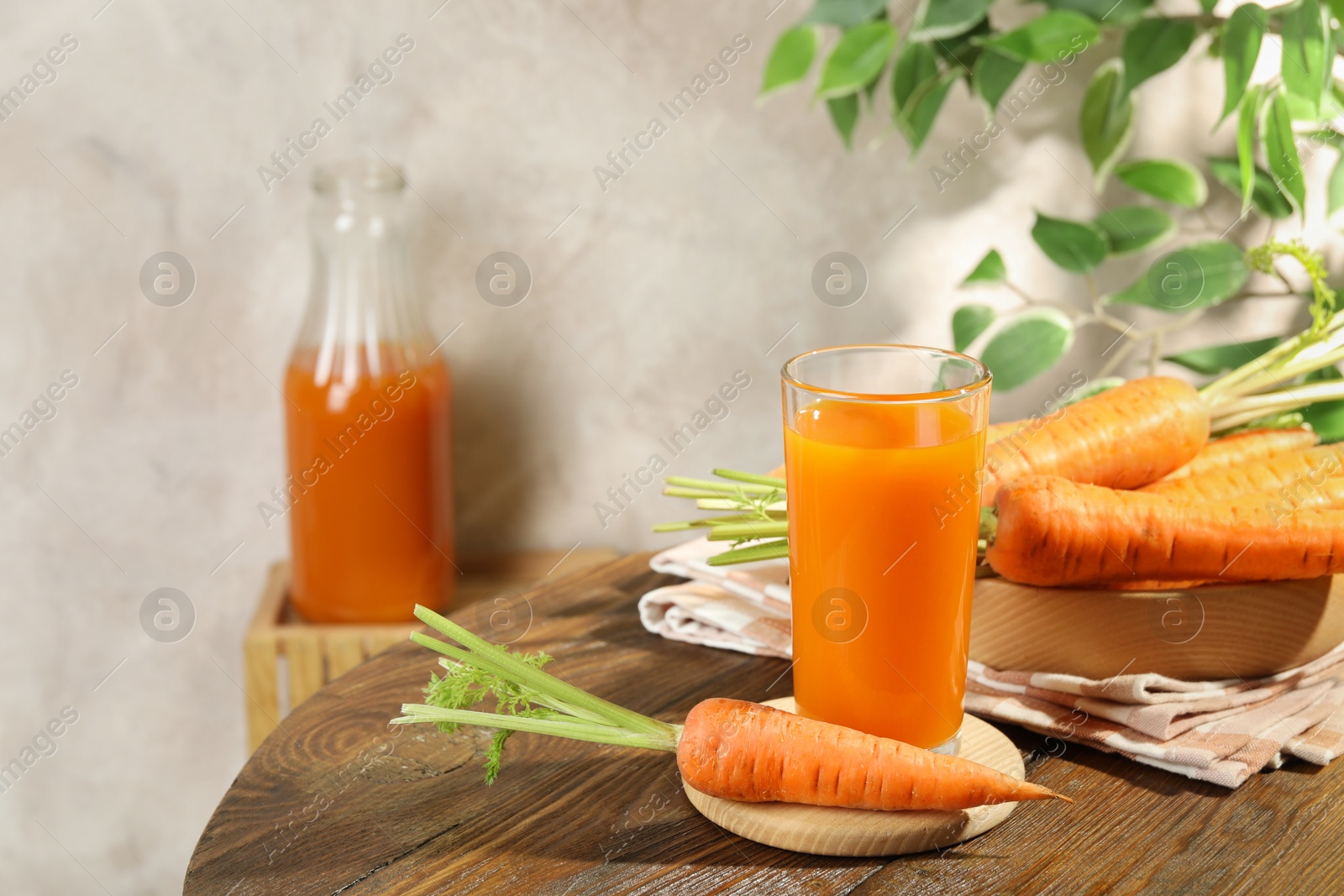 Photo of Healthy carrot juice in glass and fresh vegetables on wooden table