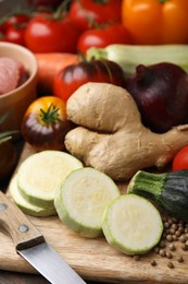 Photo of Cooking tasty stew. Fresh zucchini, ginger, tomatoes and knife on table