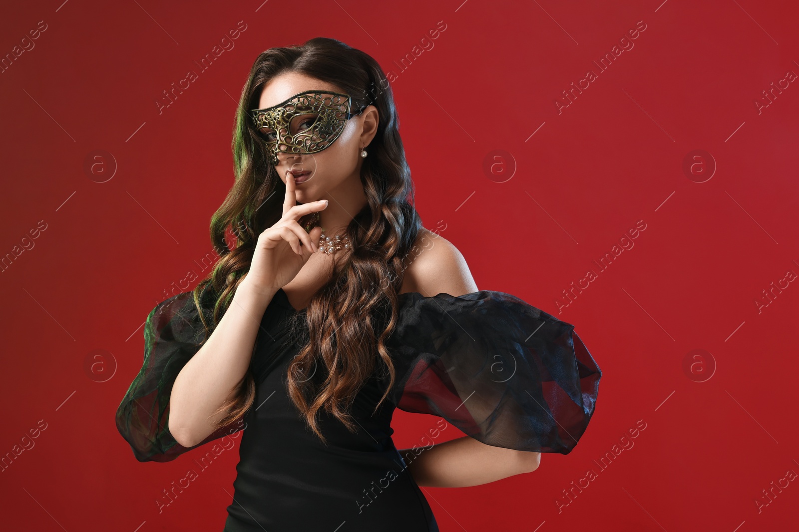 Photo of Beautiful woman with carnival mask showing hush gesture on red background in color lights. Space for text