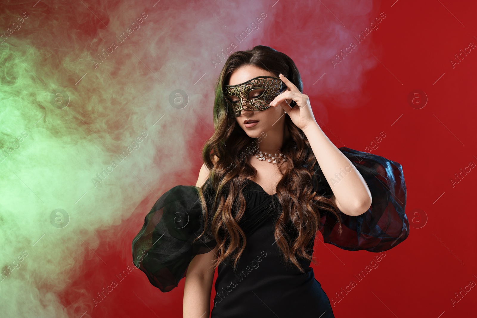 Photo of Beautiful woman wearing carnival mask on red background in color lights and smoke