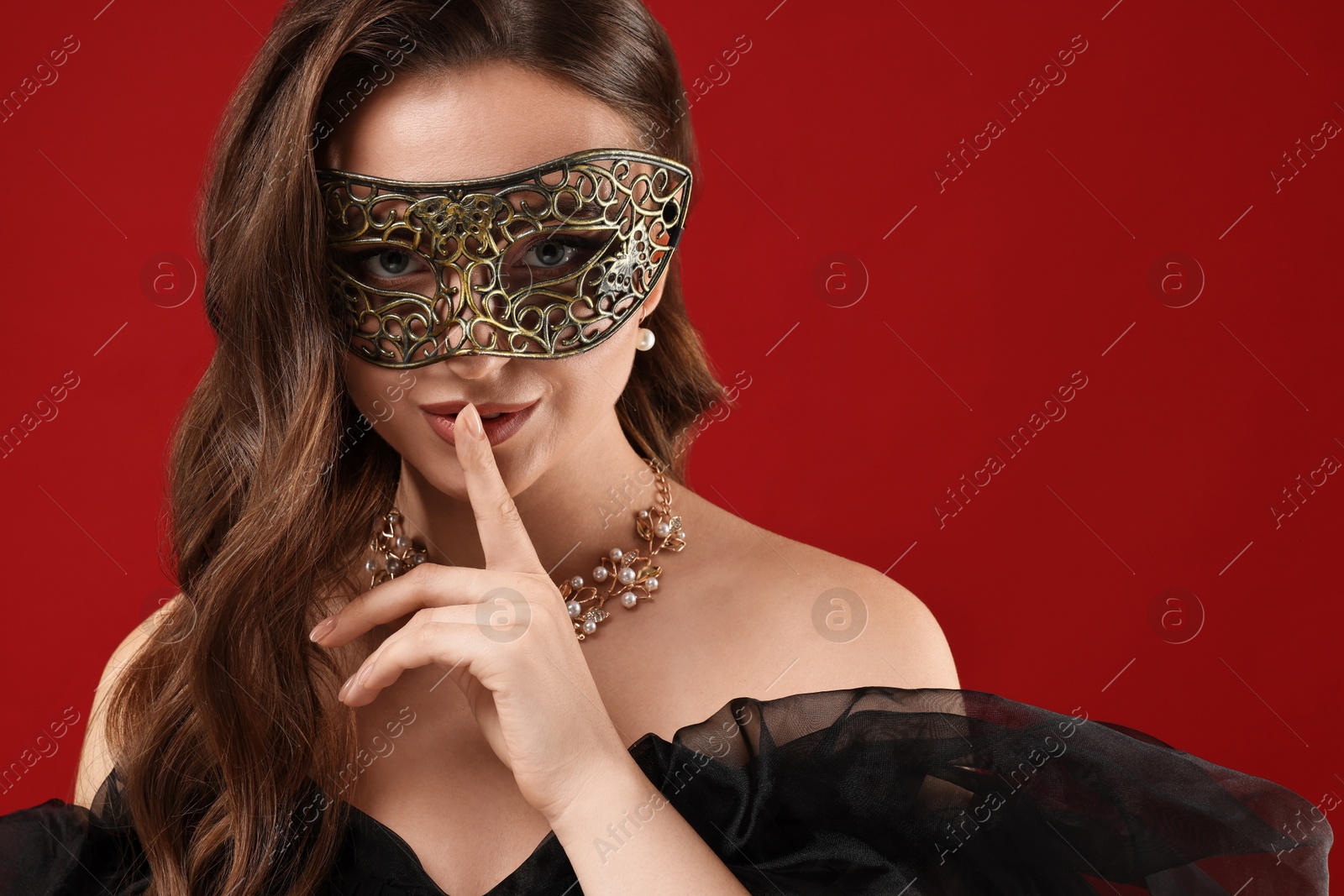 Photo of Beautiful woman with carnival mask showing hush gesture on red background. Space for text