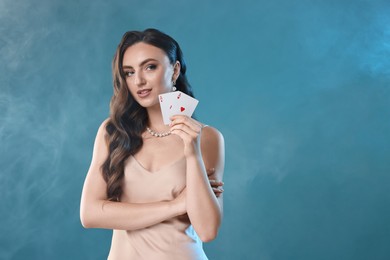 Poker game. Charming woman holding playing cards on light blue background with smoke. Space for text