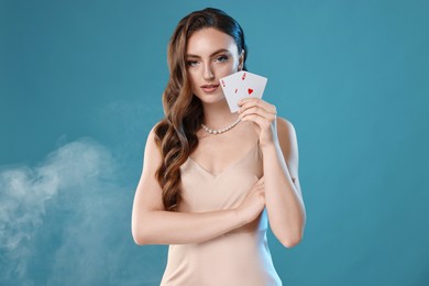 Photo of Poker game. Charming woman holding playing cards on light blue background with smoke