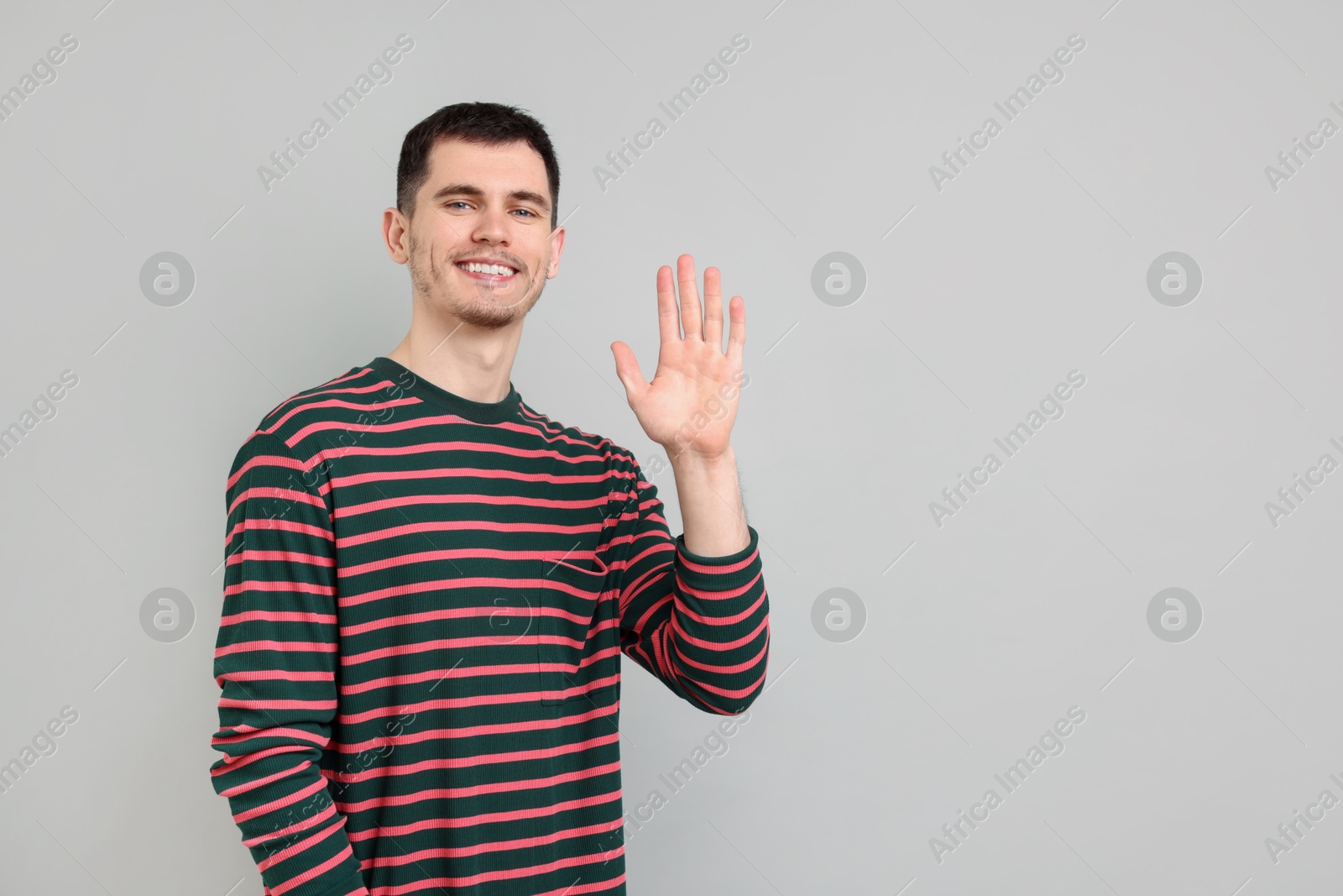 Photo of Happy young man waving on gray background, space for text