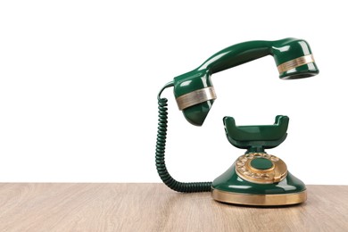 Green vintage corded telephone on wooden table against light background, space for text