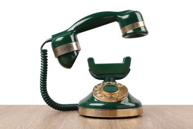 Photo of Green vintage corded telephone on wooden table against light background