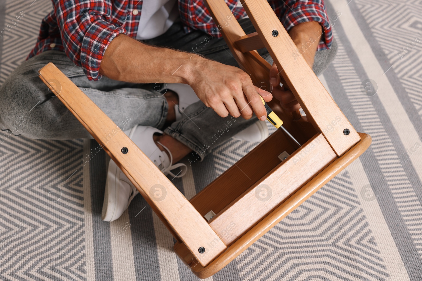 Photo of Man repairing wooden stool with screwdriver indoors, closeup