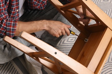 Photo of Man repairing wooden stool with screwdriver indoors, closeup