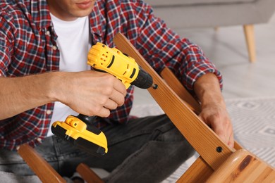 Man repairing wooden stool with electric screwdriver indoors, closeup