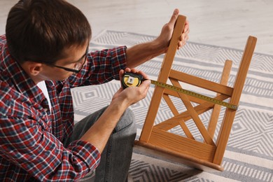 Man using tape measure while repairing wooden stool indoors