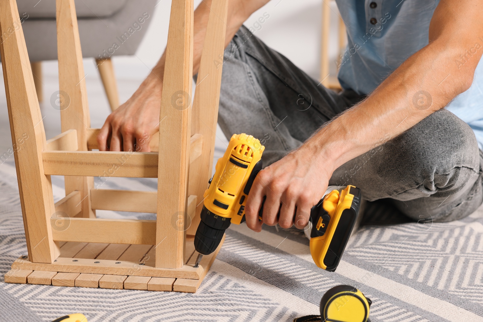 Photo of Man repairing wooden stool with electric screwdriver indoors, closeup