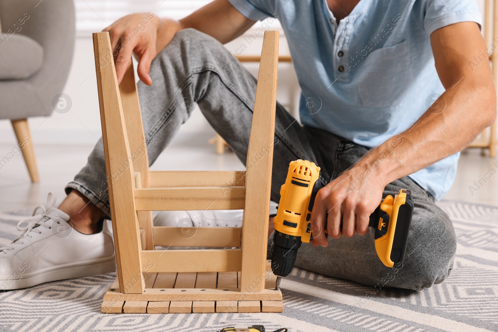 Photo of Man repairing wooden stool with electric screwdriver indoors, closeup