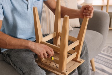 Man repairing wooden stool with screwdriver indoors, closeup