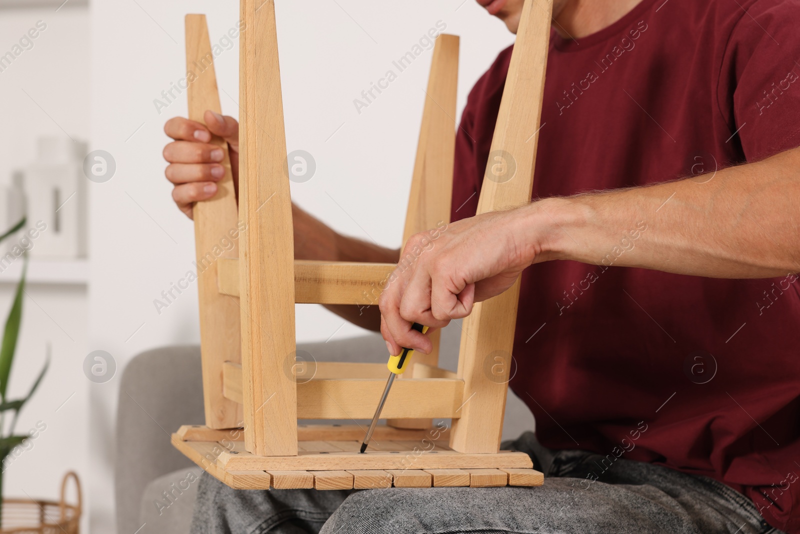 Photo of Man repairing wooden stool with screwdriver indoors, closeup