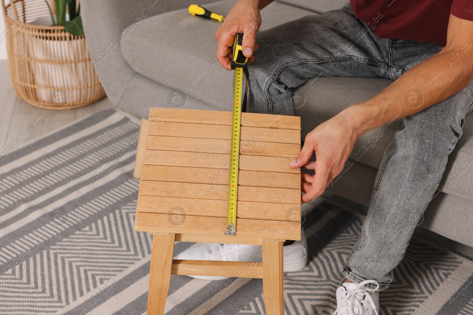 Photo of Man using tape measure while repairing wooden stool indoors, closeup