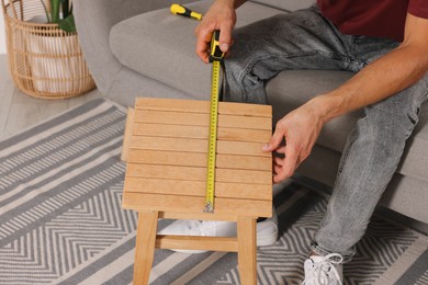 Photo of Man using tape measure while repairing wooden stool indoors, closeup