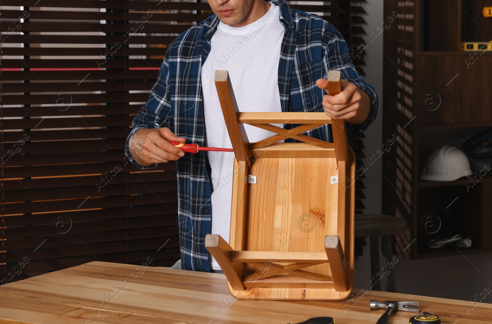 Photo of Man repairing wooden stool with screwdriver indoors, closeup