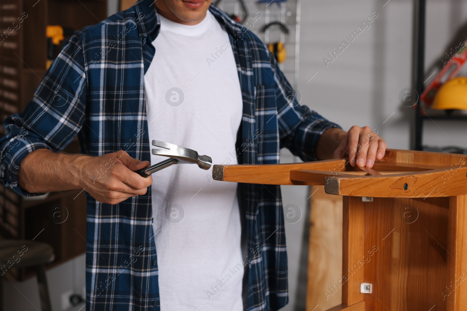 Photo of Man repairing wooden stool with hammer indoors, closeup