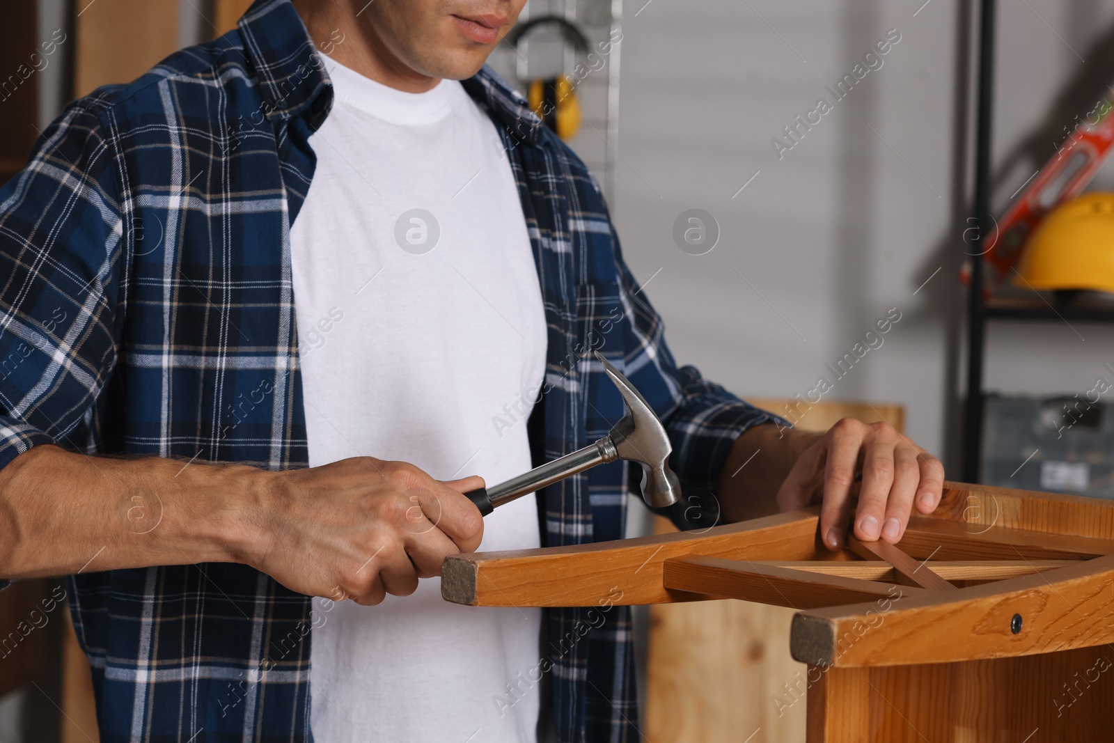 Photo of Man repairing wooden stool with hammer indoors, closeup