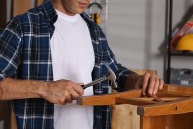 Photo of Man repairing wooden stool with hammer indoors, closeup