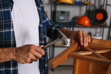 Photo of Man repairing wooden stool with hammer indoors, closeup