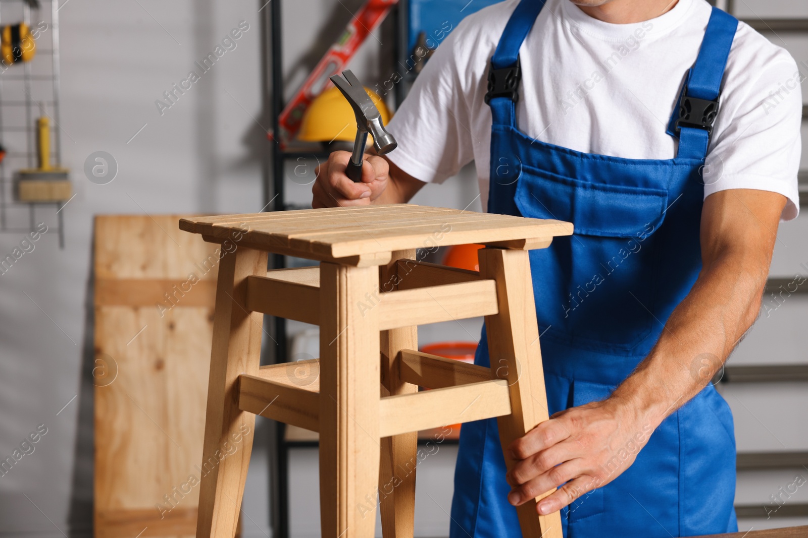 Photo of Man repairing wooden stool with hammer indoors, closeup