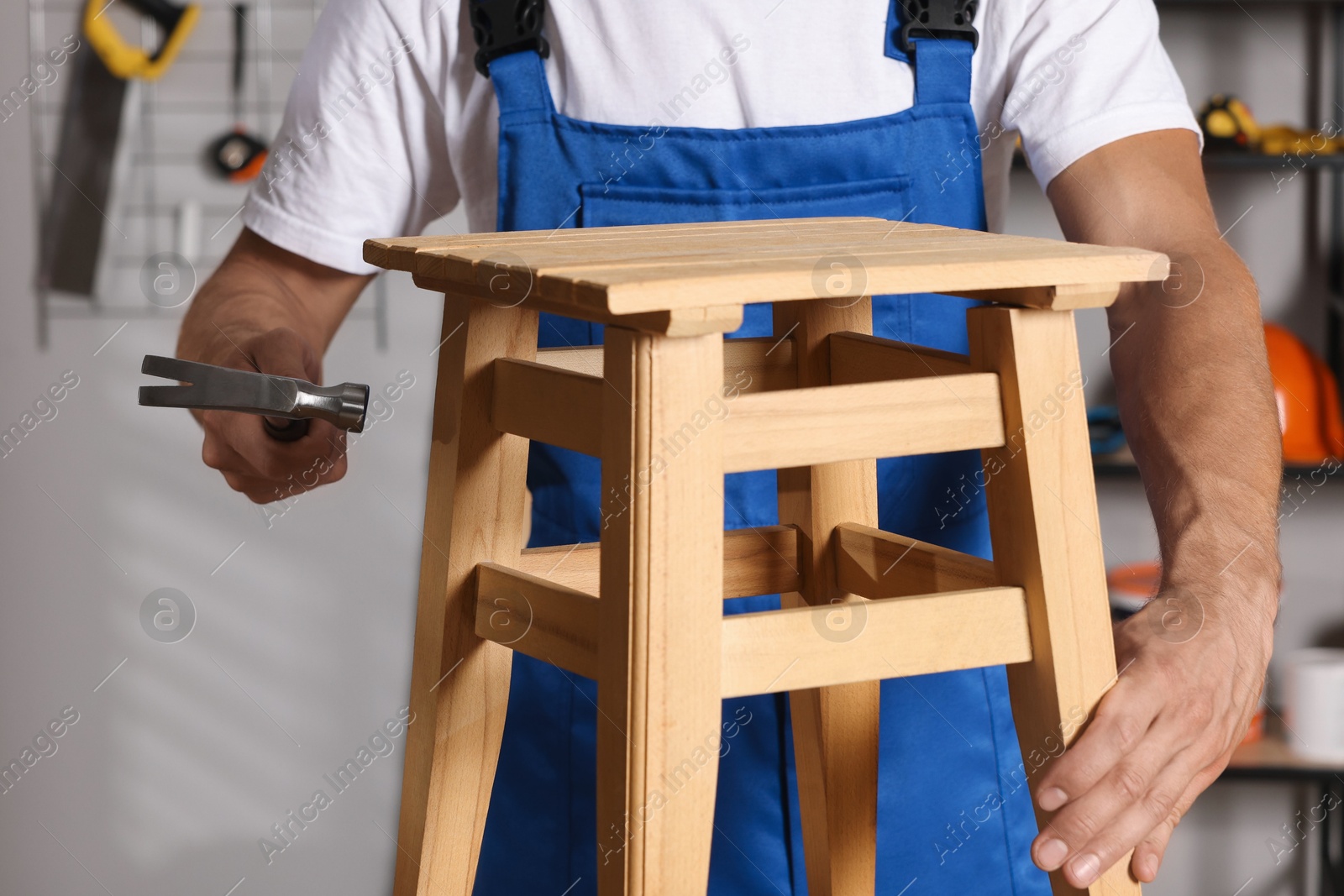 Photo of Man repairing wooden stool with hammer indoors, closeup