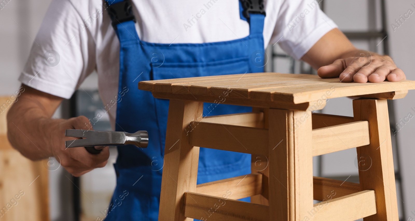 Photo of Man repairing wooden stool with hammer indoors, closeup