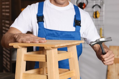 Photo of Man repairing wooden stool with hammer indoors, closeup